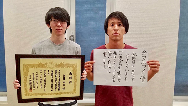 表彰状を持つ伊藤と佐々木のツーショット写真